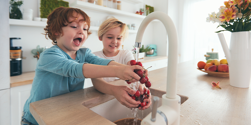 Kinder waschen Obst unter Leitungswasser